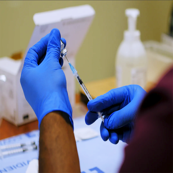 pair of blue vinyl-gloved hands filling a syringe with vaccine
